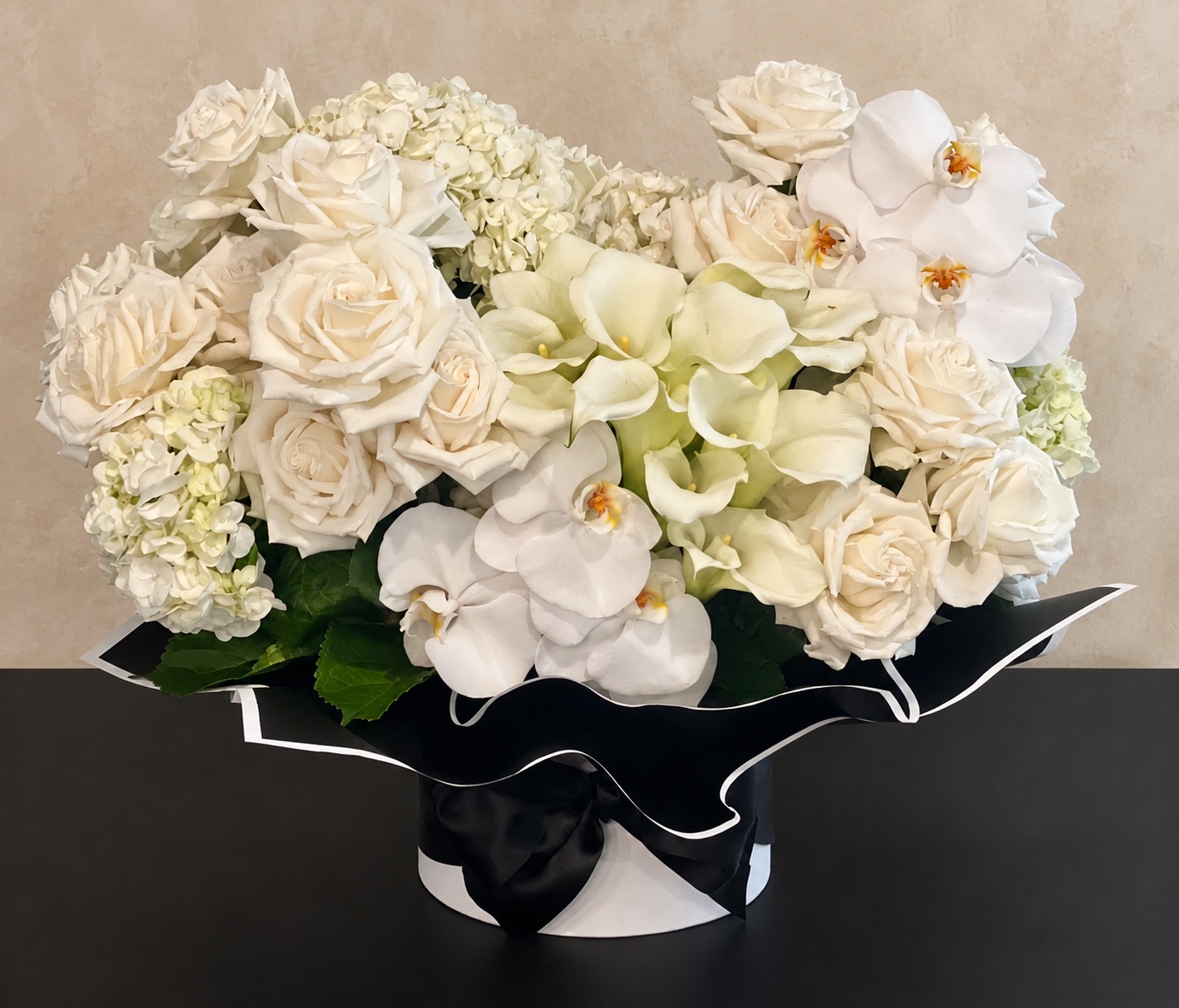 Luxurious ivory roses, hydrangeas, white orchids, and calla lilies arranged in black and white wrapping