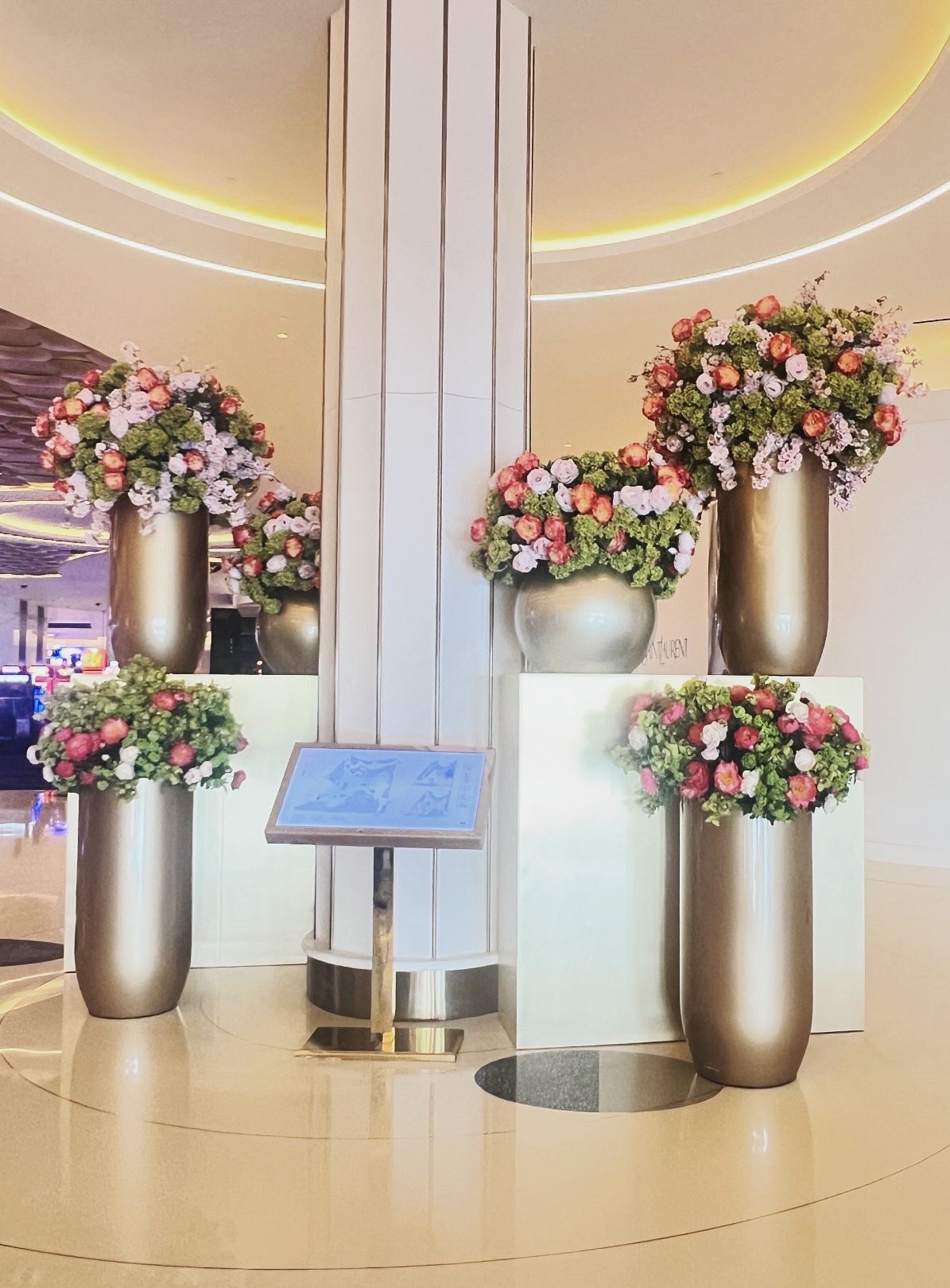 Pink, coral, and green floral arrangements in tall bronze vessels of different heights within a luxury interior