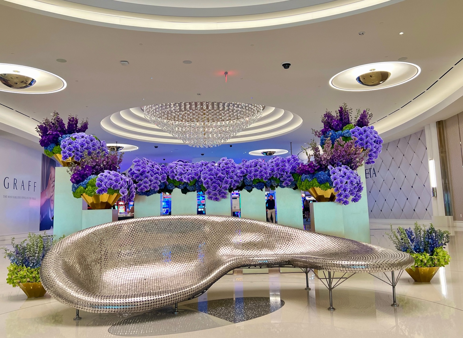Large-scale lavender and deep purple orchid installation surrounding a curved reflective seating sculpture