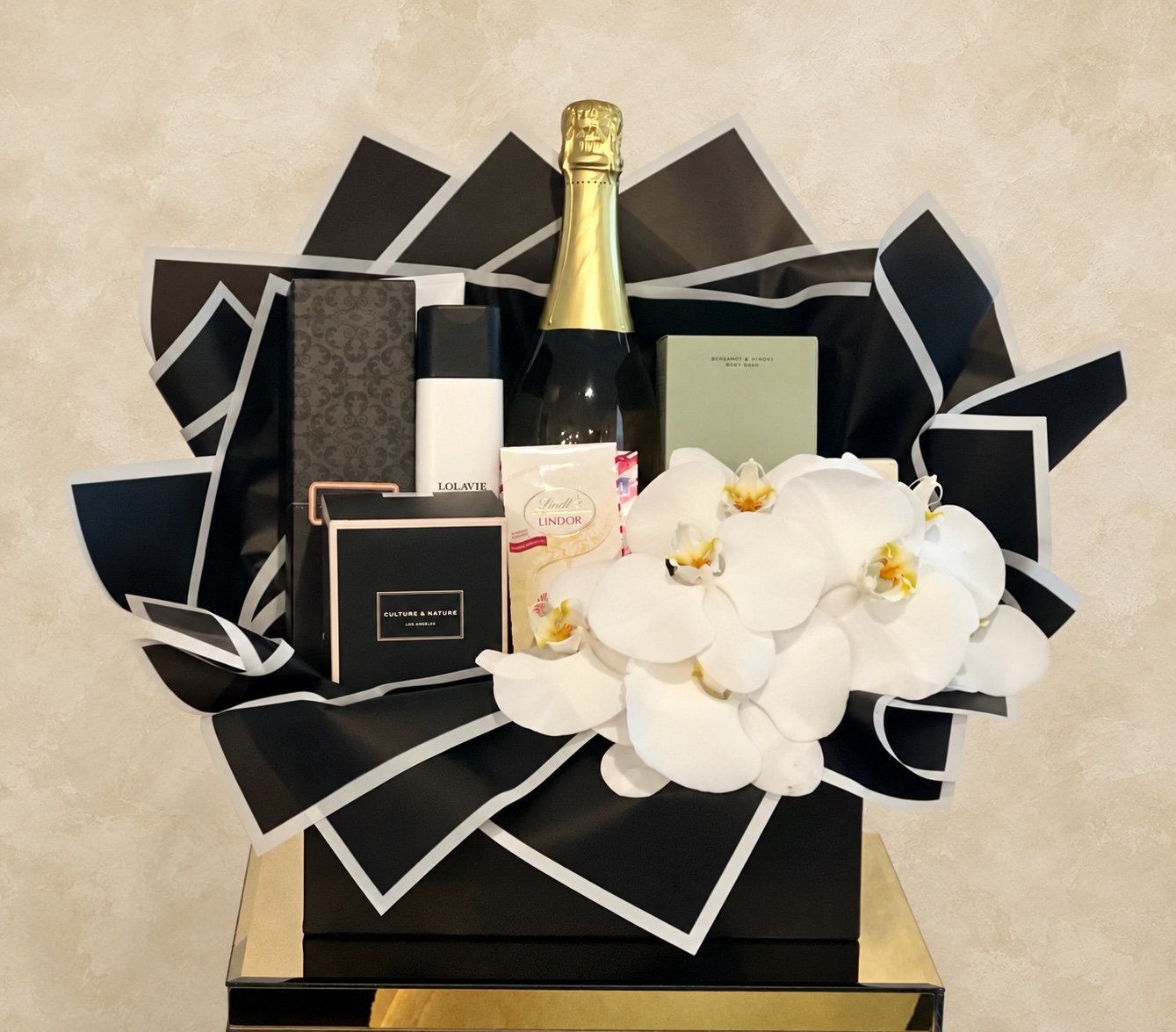 Luxury gift presentation with black and white folded packaging, white orchids, champagne, and curated gifts